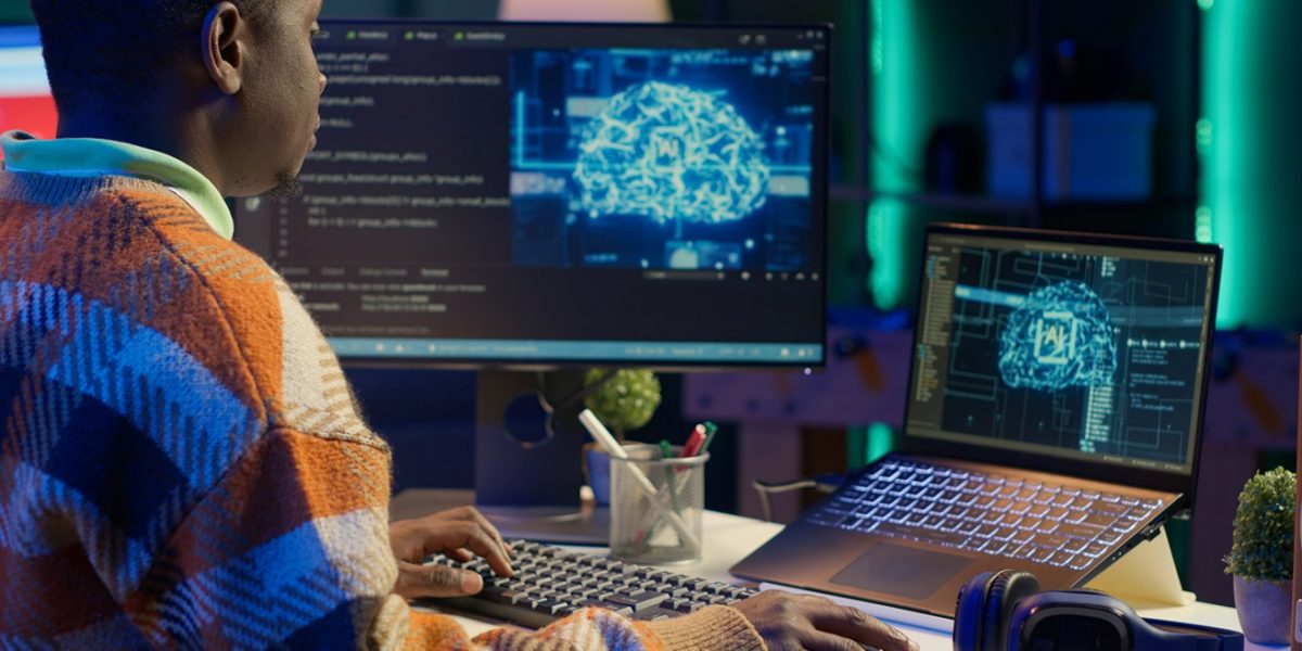 Black man programmer manages code and scripts in artificial intelligence and machine learning on dual monitors pc. Male freelancer uses personal computer to guarantee cyber security. Camera A.